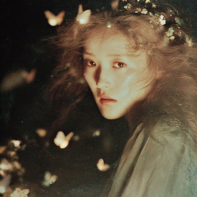 A person with luminous eyes and flowing hair immersed in glowing butterflies and flower petals, half in shadow and half in golden light, with an expression of wonder