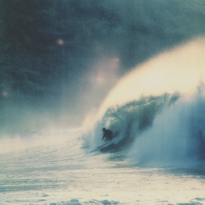 A surfer riding an enormous wave, suspended in perfect balance as the massive curl of water forms a tunnel around them, with ocean spray catching sunlight